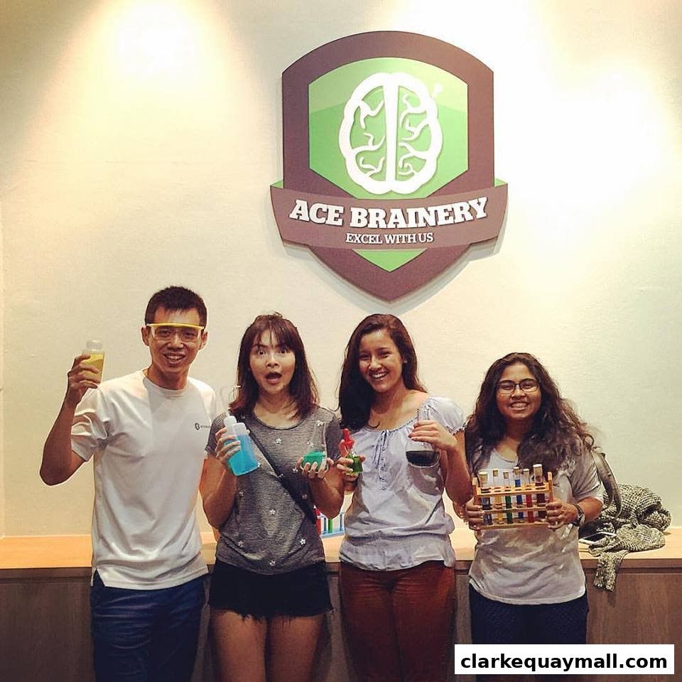 Four smiling people stand in front of the Ace Brainery logo, holding science experiment materials.
