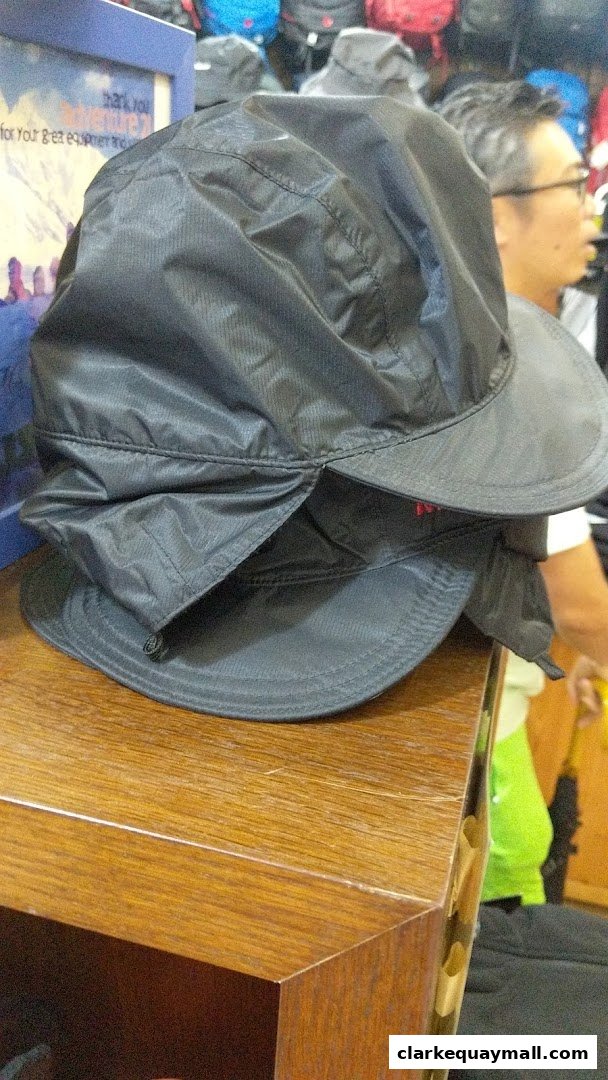 Close-up of black outdoor hats stacked on a wooden shelf with a sign in the background.