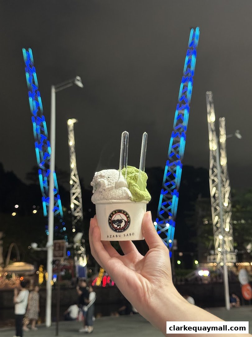 A hand holds a cup of gelato with two flavors, with illuminated towers in the background.