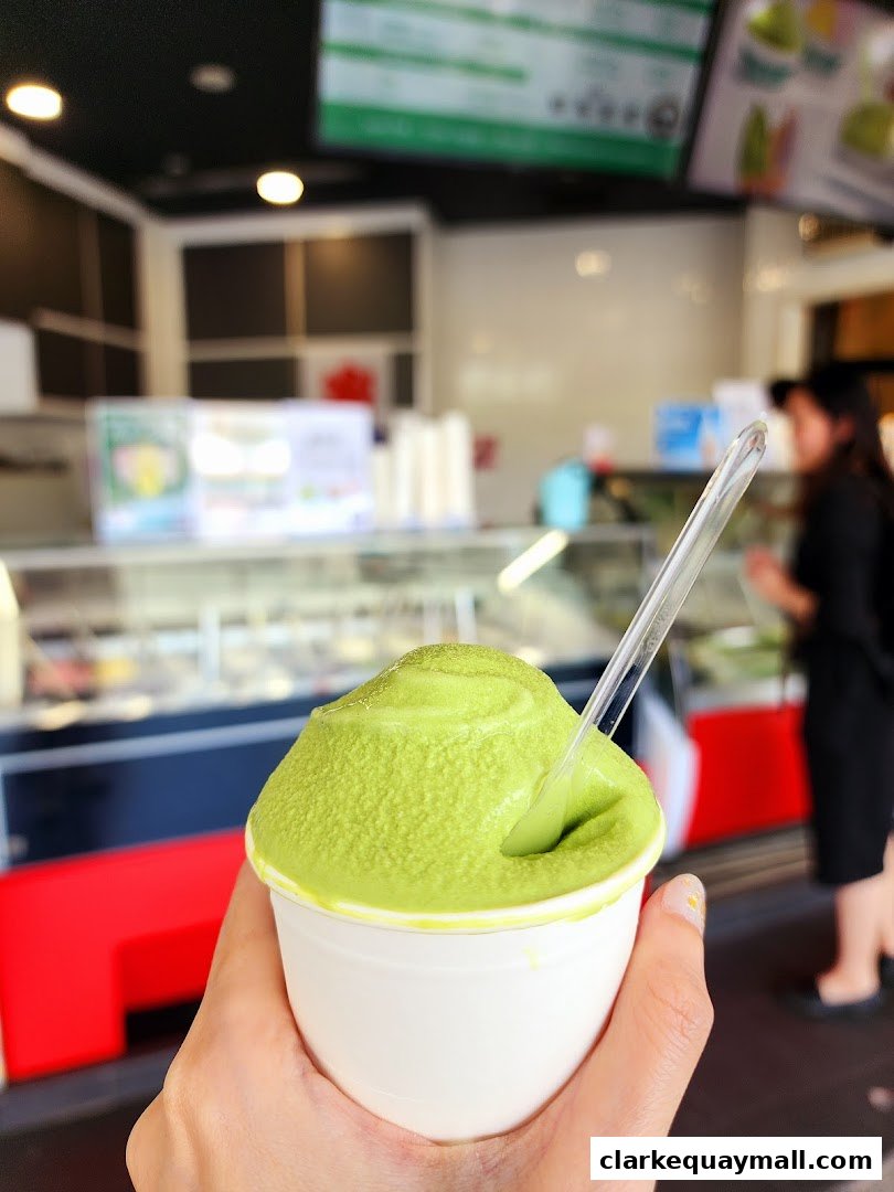 A hand holds a cup of vibrant green matcha soft serve ice cream.