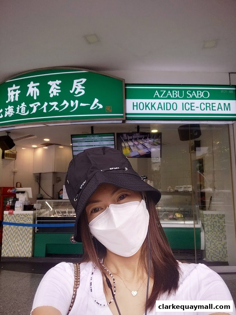 A person wearing a mask and hat poses in front of the Azabu Sabo Hokkaido Ice-Cream shop.