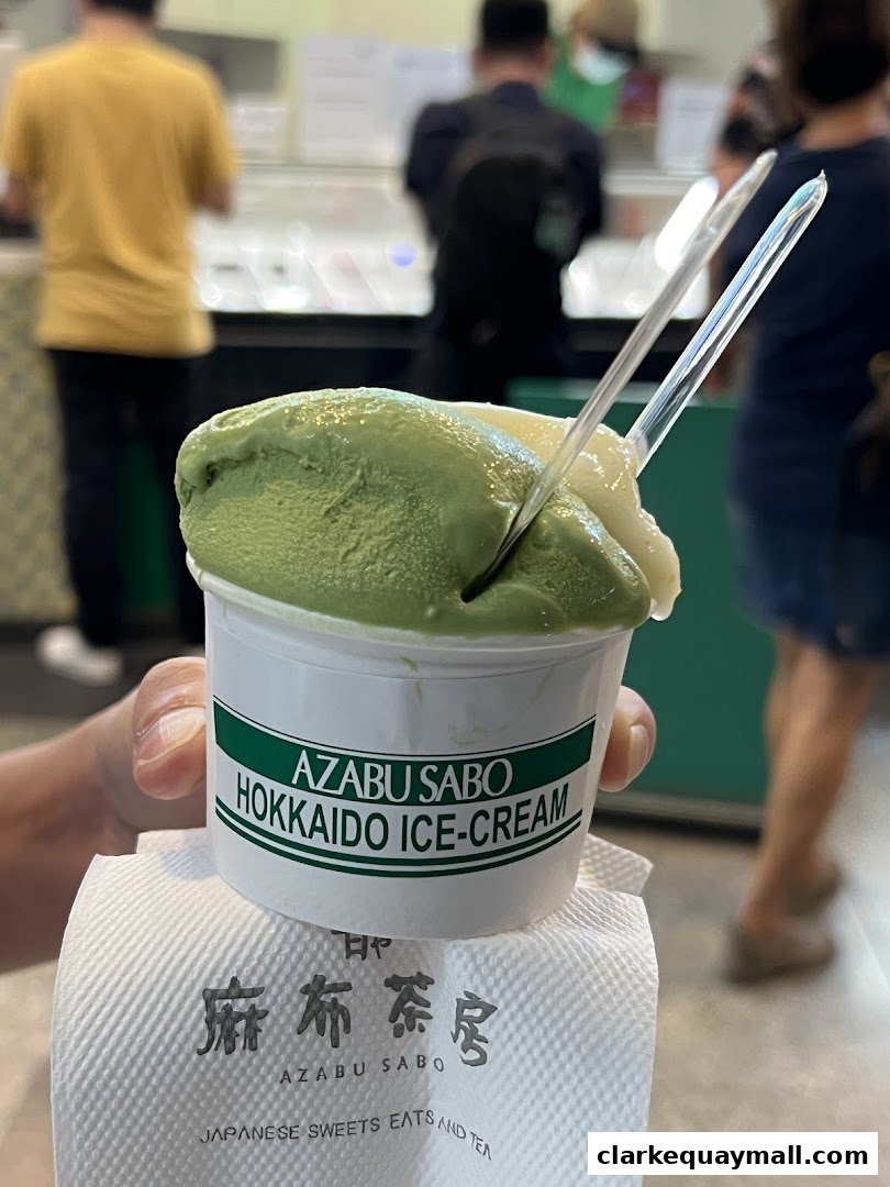 A hand holds a cup of Hokkaido ice cream with green and white scoops.