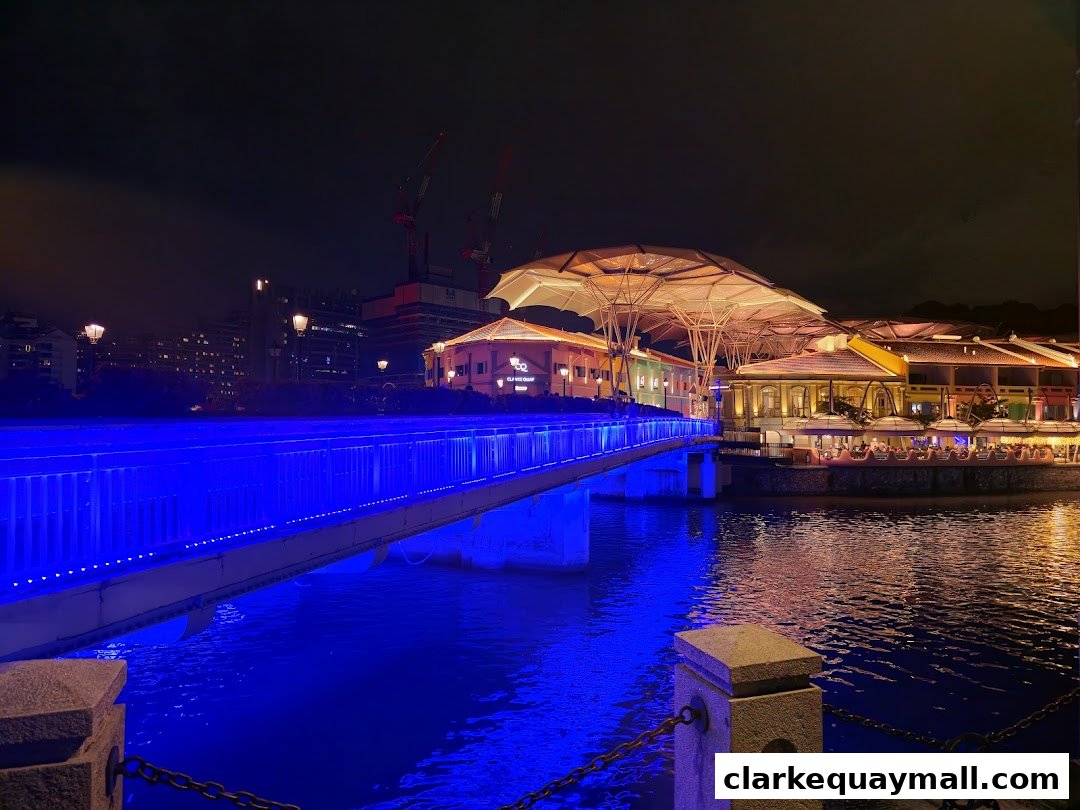 A vibrant night view of Clarke Quay with a bridge illuminated by blue lights.