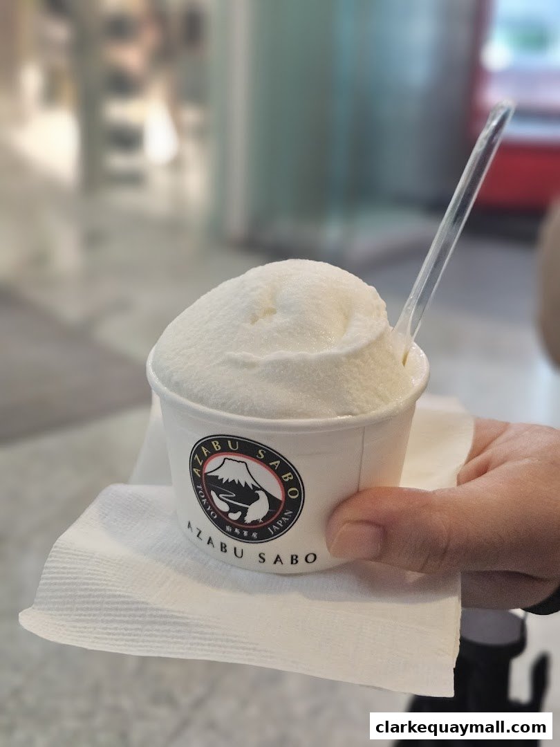 A hand holds a cup of white ice cream with a spoon from Azabu Sabo.