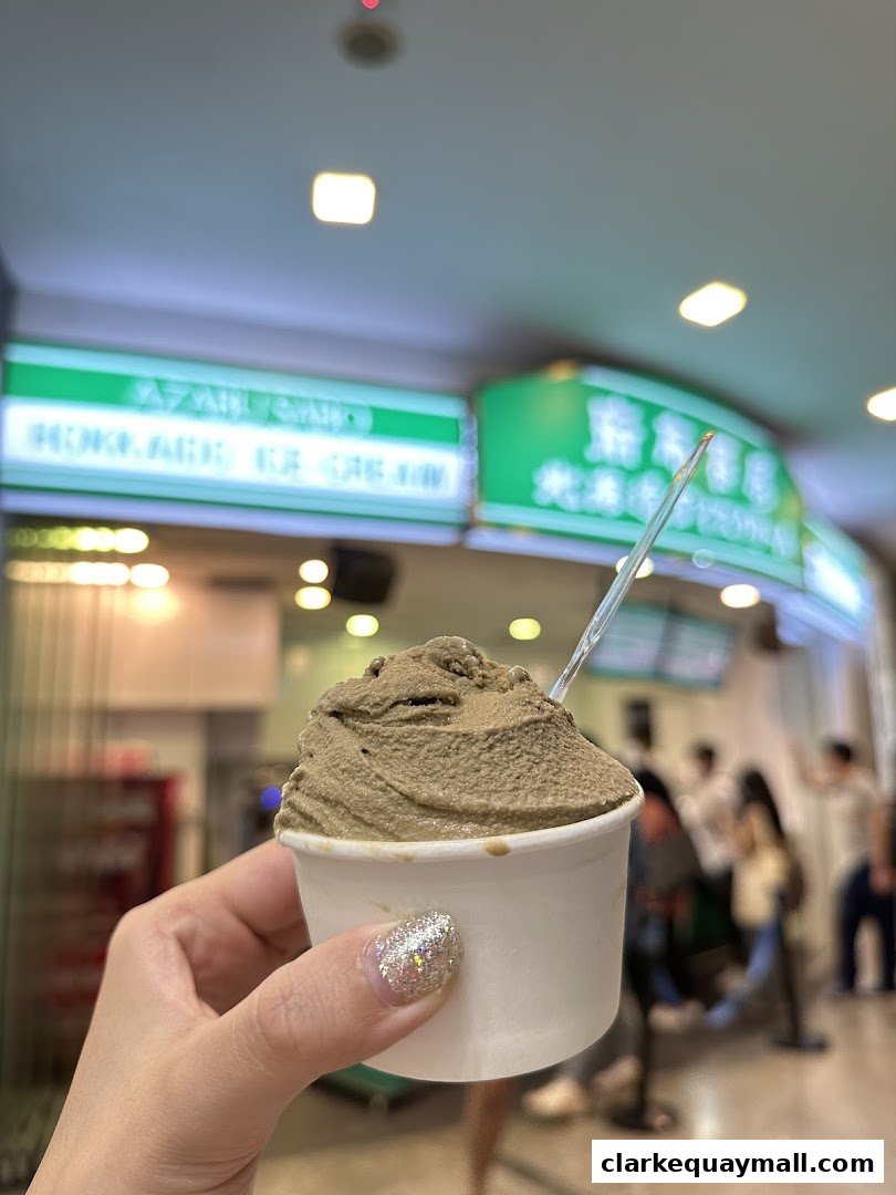 A hand holds a cup of ice cream in front of the Azabu Sabo Hokkaido Ice Cream shop.