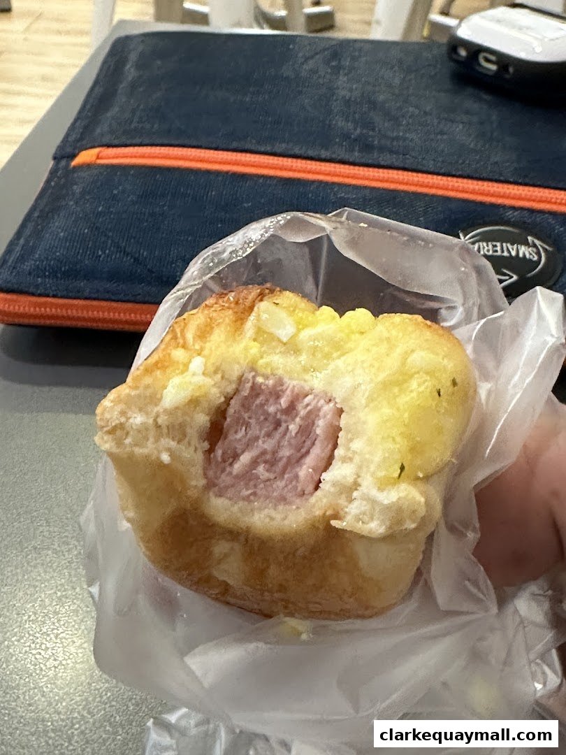 A close-up shot of a pastry with a sausage filling, held in plastic packaging.