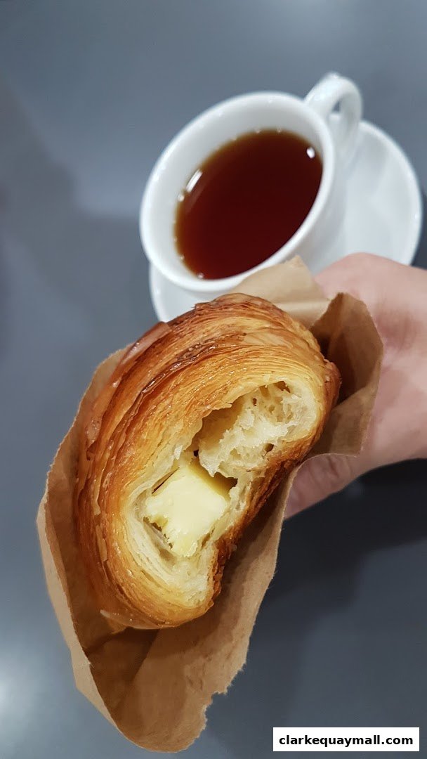 A hand holds a flaky croissant filled with butter next to a cup of tea.
