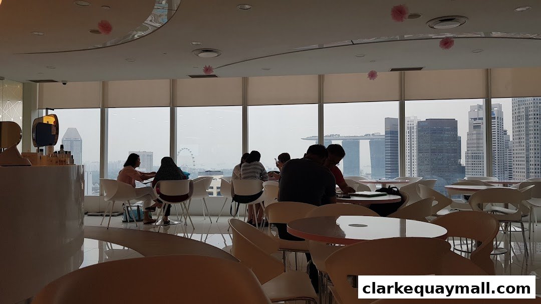 Interior of a modern cafe with people seated at tables, overlooking a city skyline.