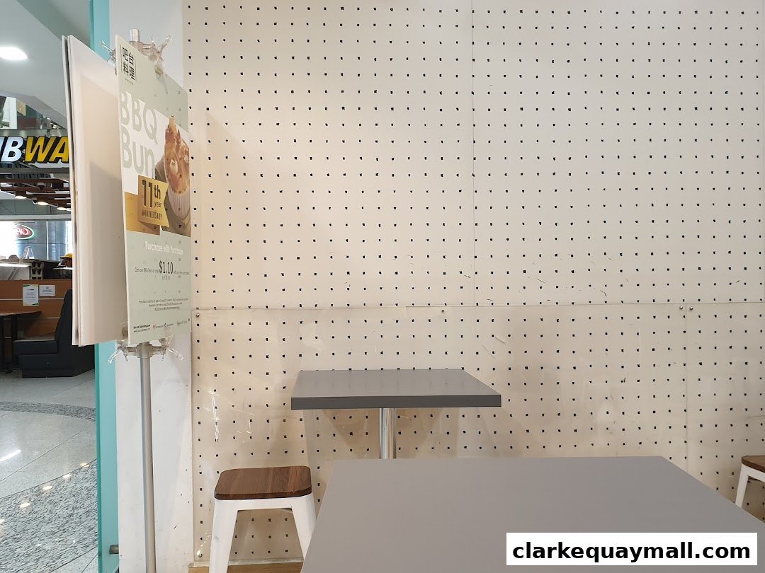 A promotional sign for BBQ Bun from Barcook Bakery is displayed next to tables and chairs.
