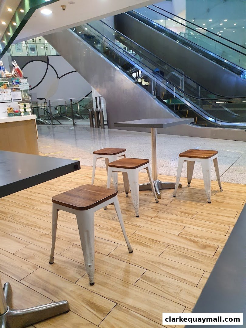 Seating area with tables and stools in front of escalators at Barcook Bakery.