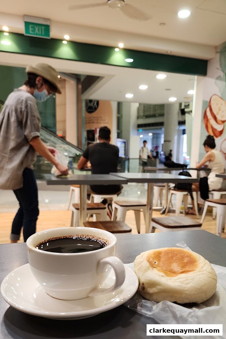 A cup of coffee and a pastry are on a table in a bakery with people dining.