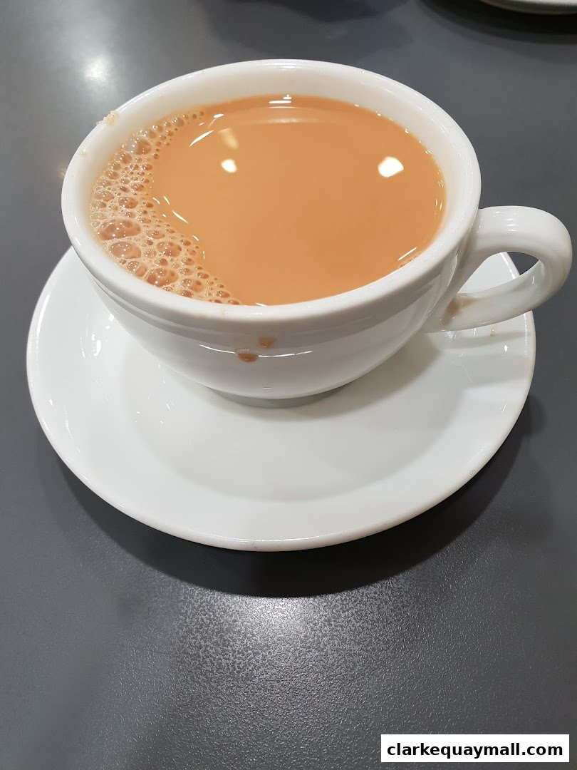 A close-up shot of a steaming cup of milk tea with foam on a white saucer.
