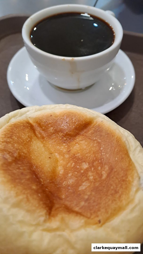 A close-up shot of a freshly baked bun and a cup of black coffee.