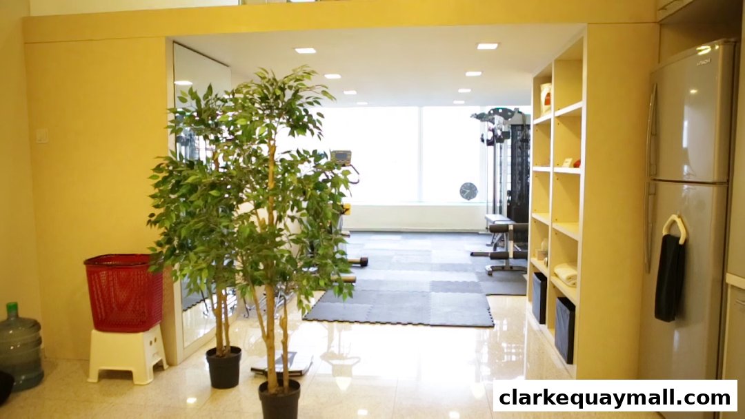 Interior view of a gym with exercise equipment, plants, and a refrigerator.