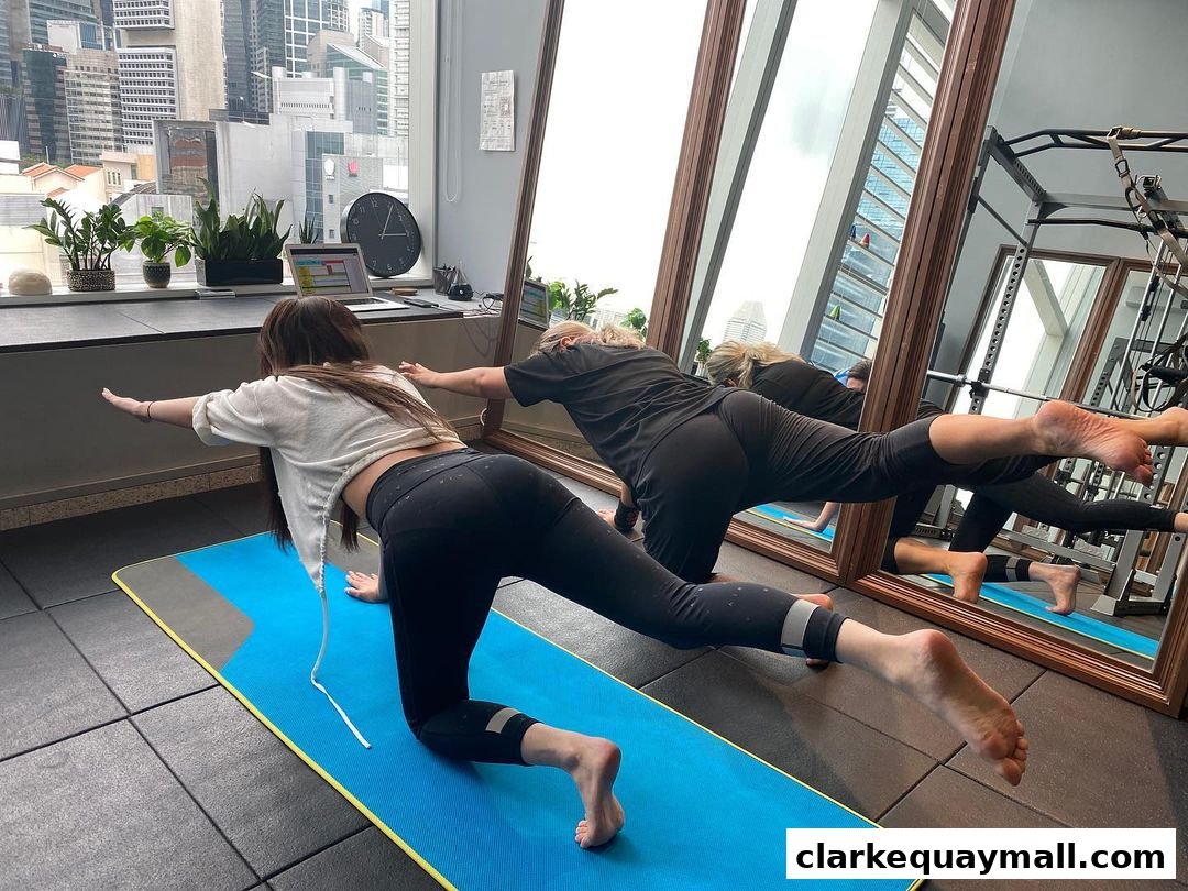 Two women practicing yoga poses on mats in a bright studio with city views.