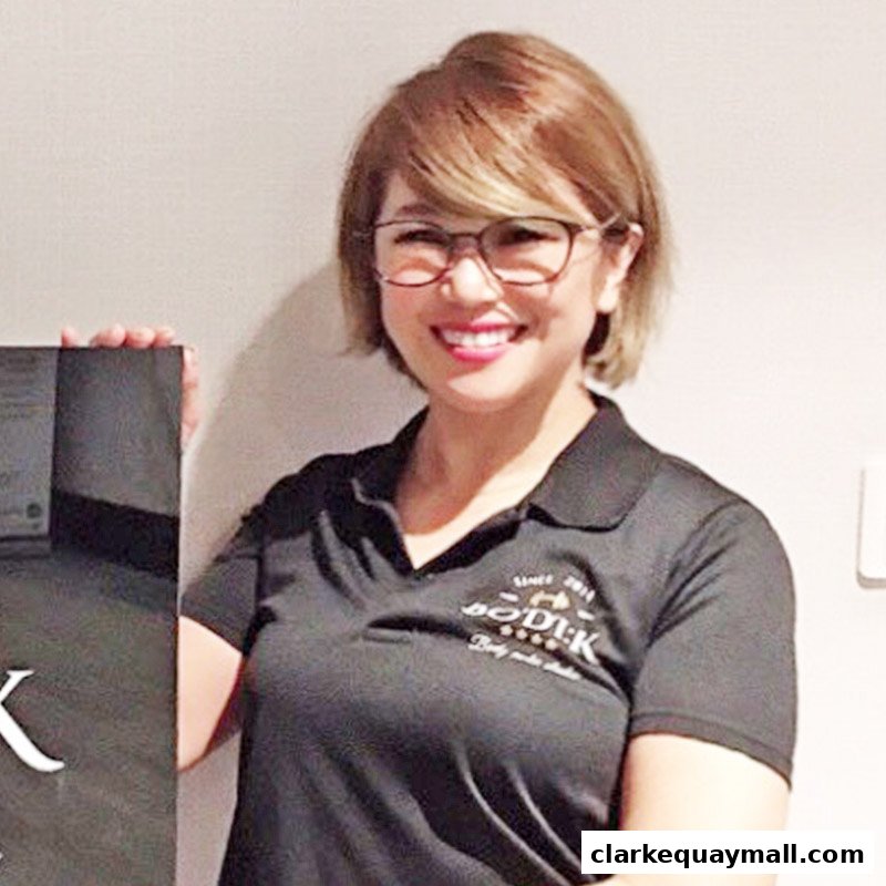 A smiling woman wearing a black polo shirt with the BODIK logo holds a dark sign.