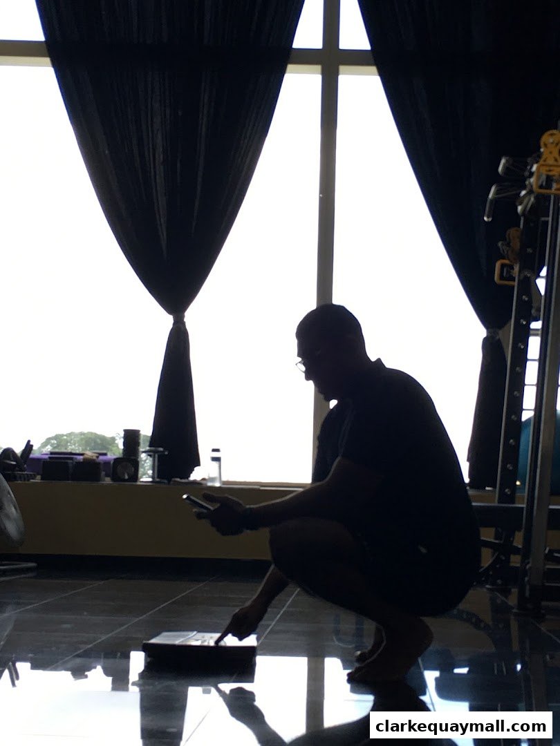 A person squats in a gym, interacting with a device on the floor.
