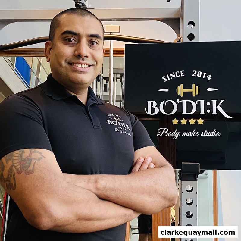 A man in a black polo shirt with the BODIK logo stands with his arms crossed.