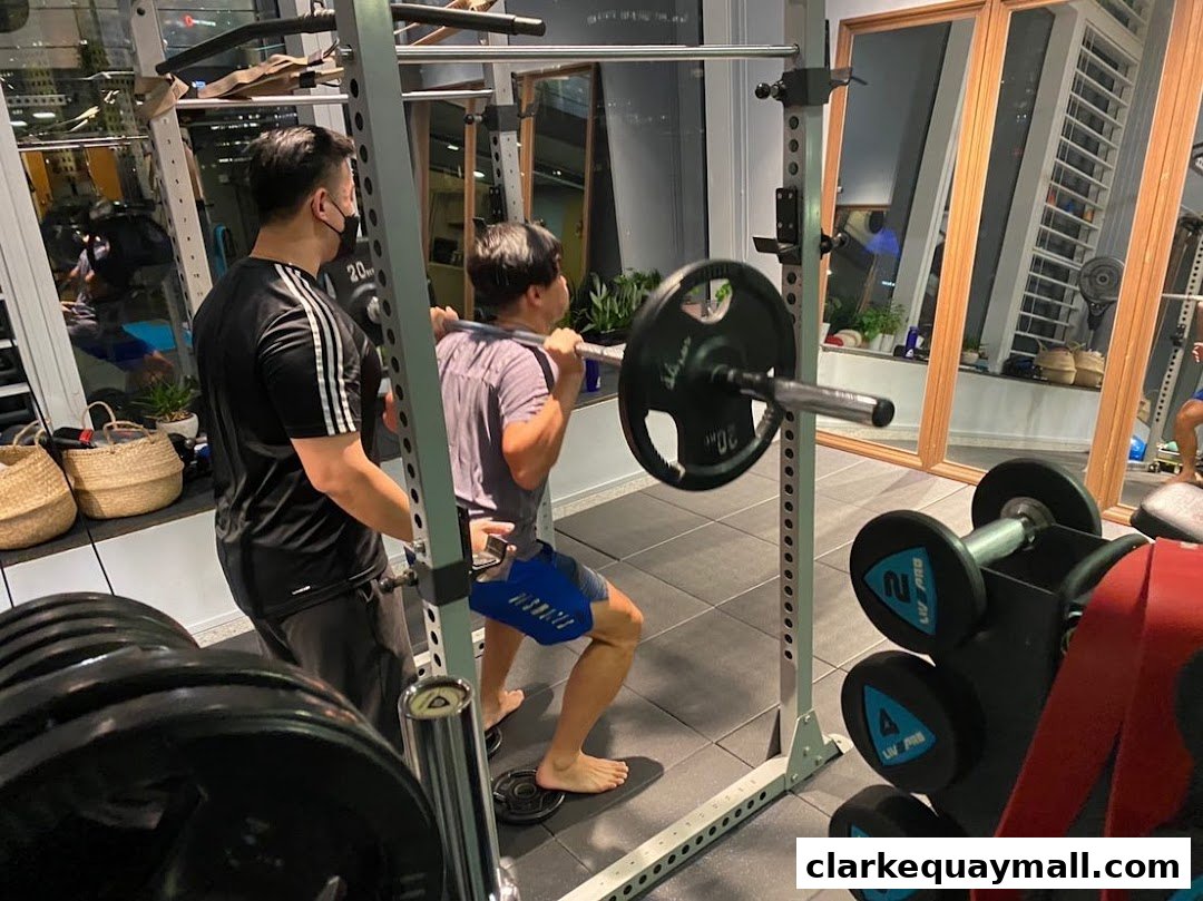 A trainer assists a client performing a barbell squat in a gym.