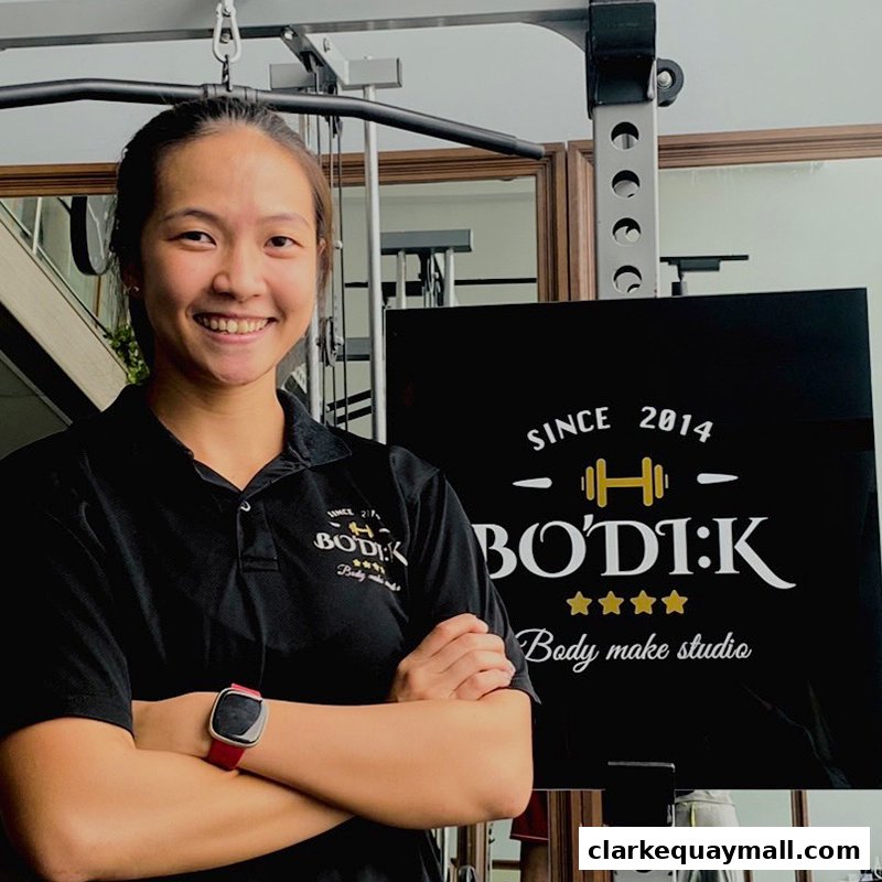 A smiling woman in a black polo shirt stands with her arms crossed in a gym.