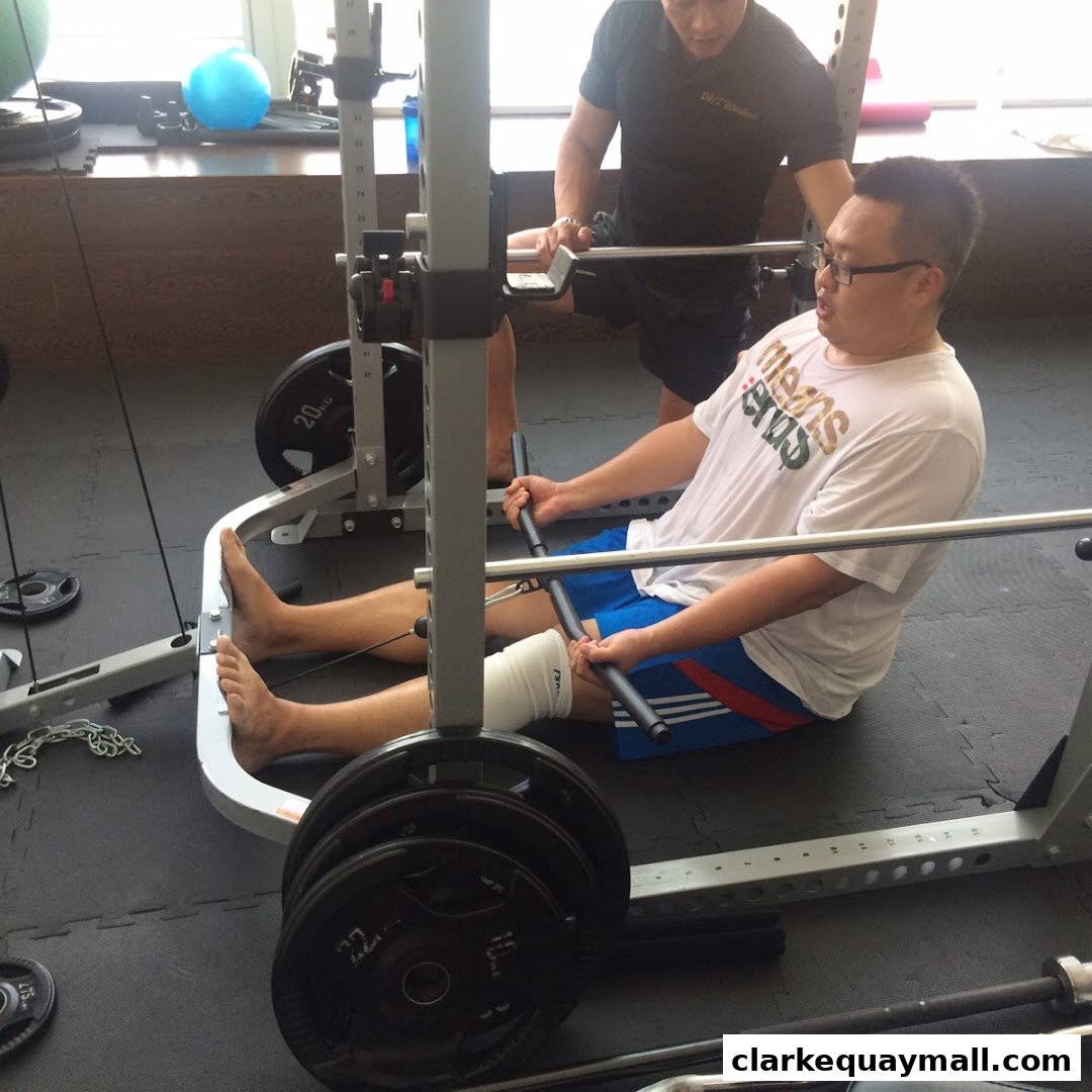 A man is assisted by a trainer while performing a leg exercise with weights.