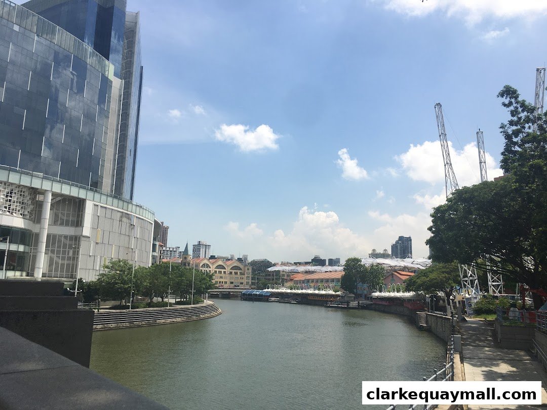 A scenic view of a riverfront with modern buildings and lush trees under a blue sky.