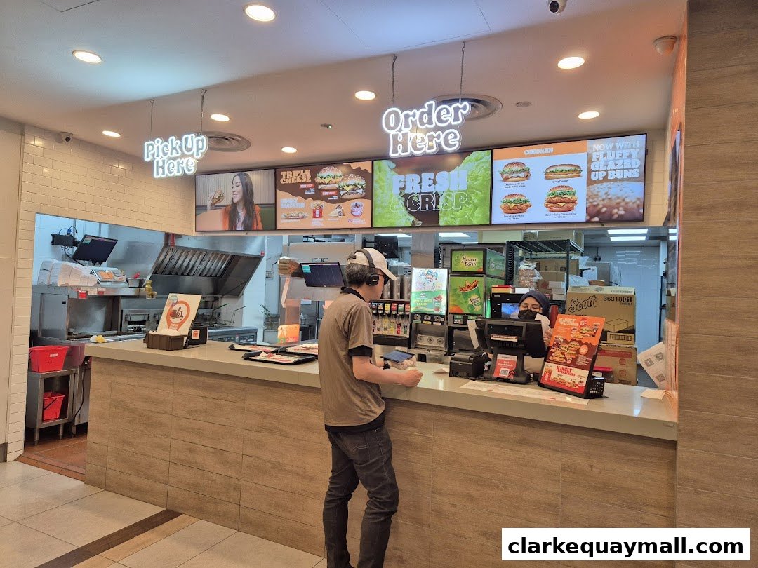 Burger King counter with staff serving customers and digital menu boards displaying food.