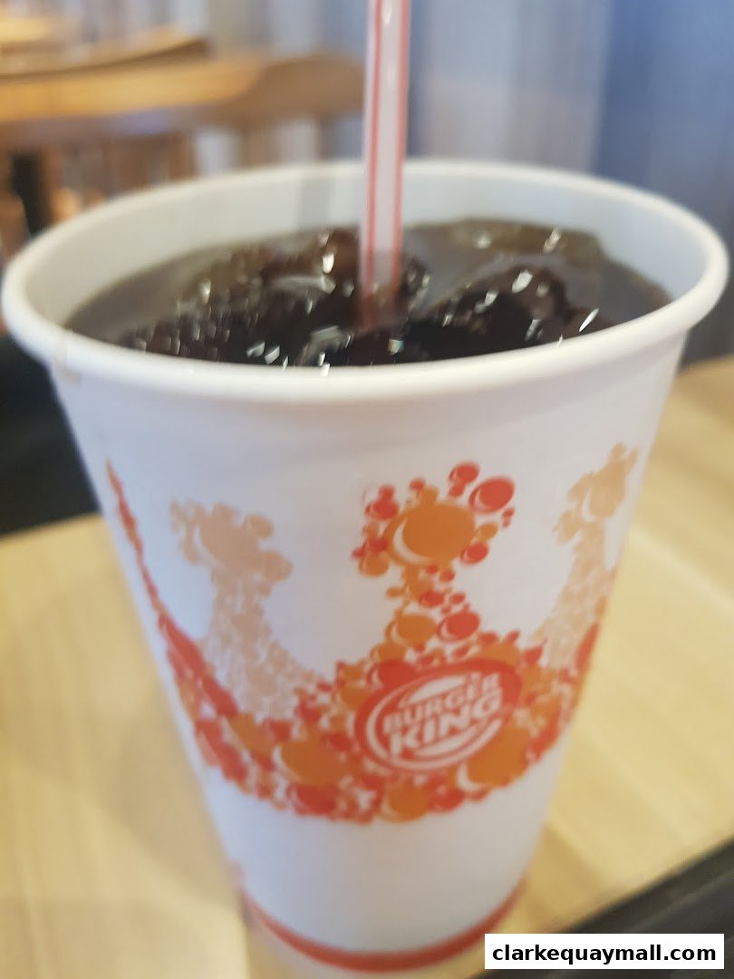 A close-up of a Burger King branded cup filled with a dark beverage and ice, with a straw.
