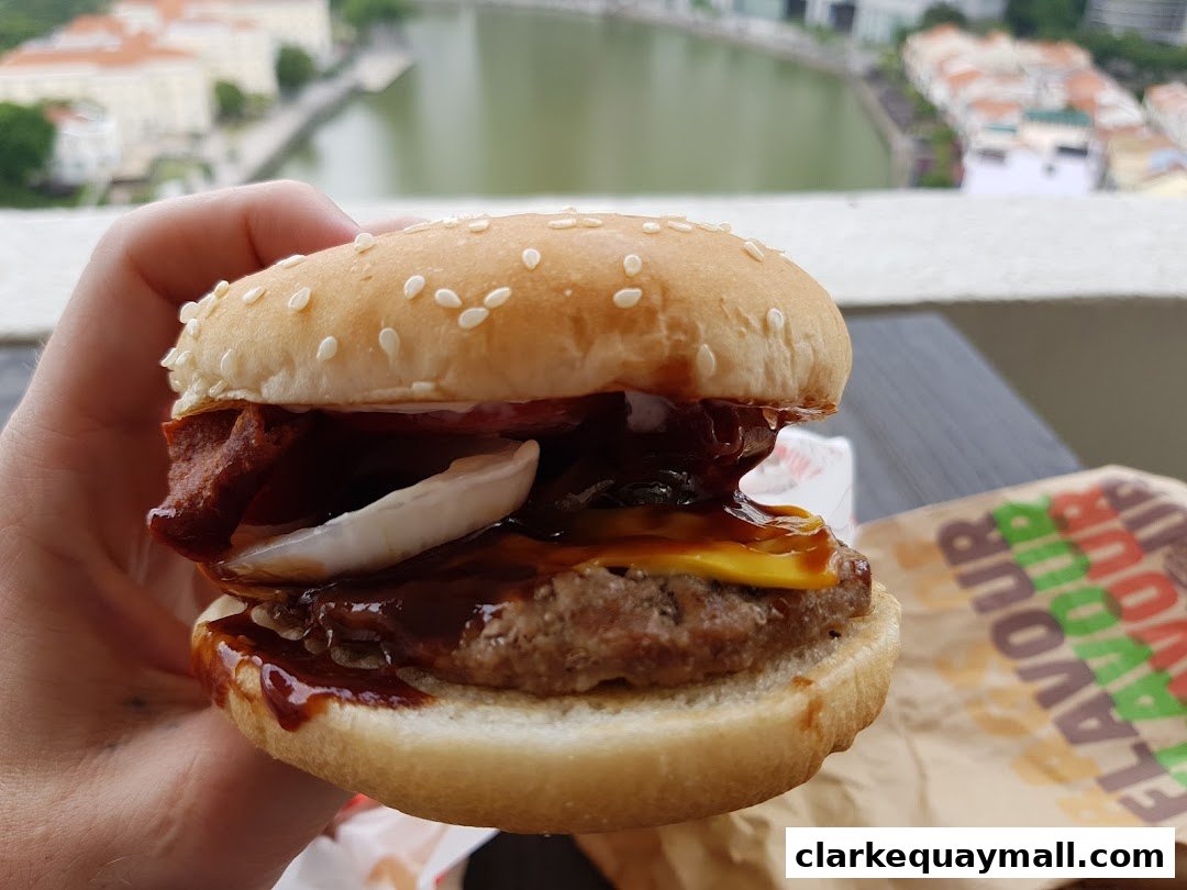 A hand holds a juicy Burger King burger with barbecue sauce and cheese.