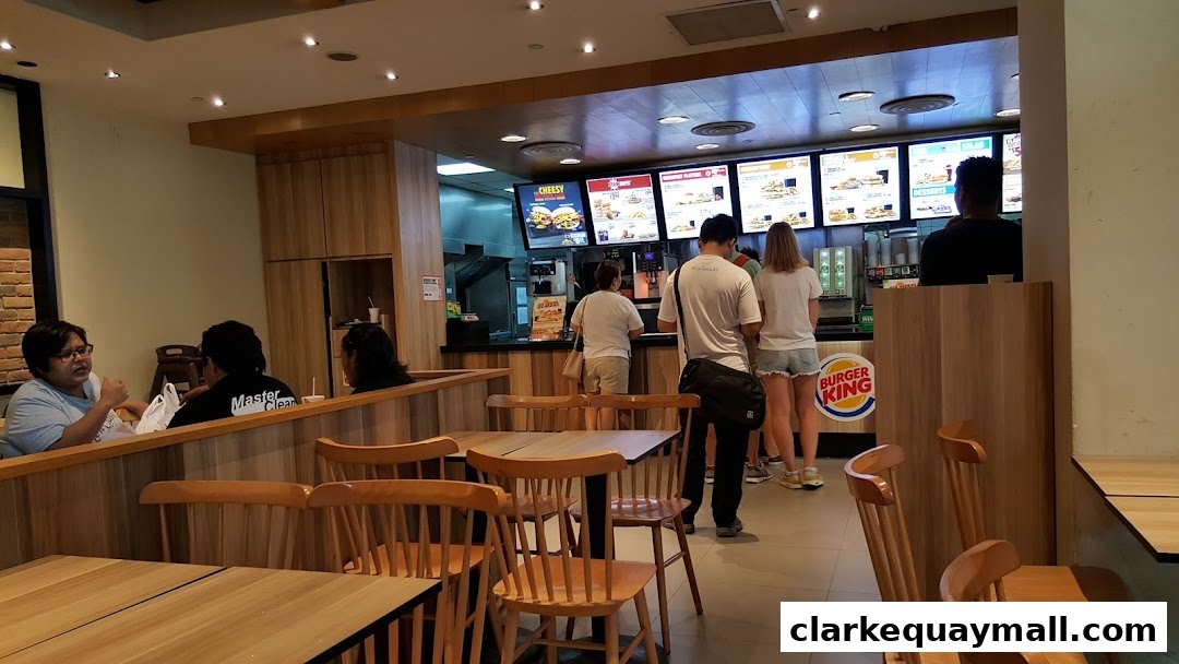 Customers queue at the counter of a Burger King restaurant with digital menus above.