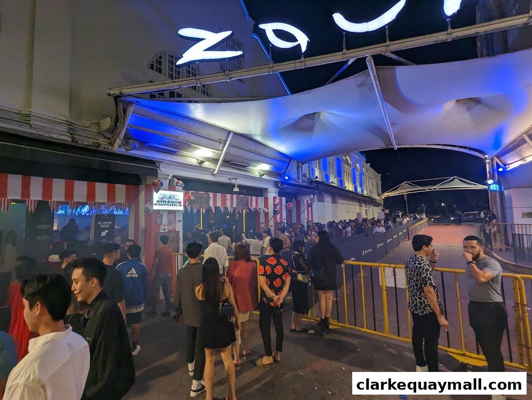 A crowd of people queuing outside a brightly lit establishment at night.