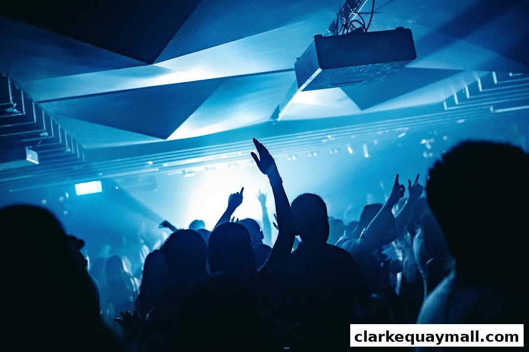 A crowd of people with their hands raised in a dimly lit club with blue lighting.