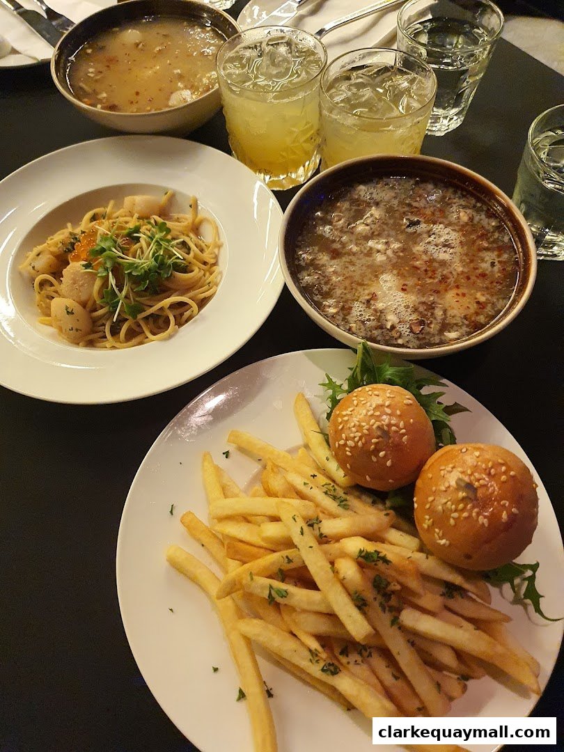 A table laden with delicious food and drinks, including pasta, fries, sliders, and soup.