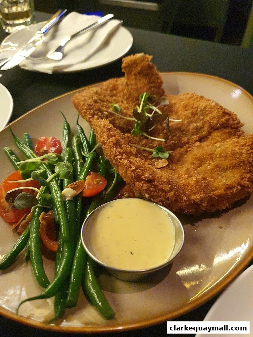 A plate of crispy fried chicken with green beans, tomatoes, and a side of sauce.