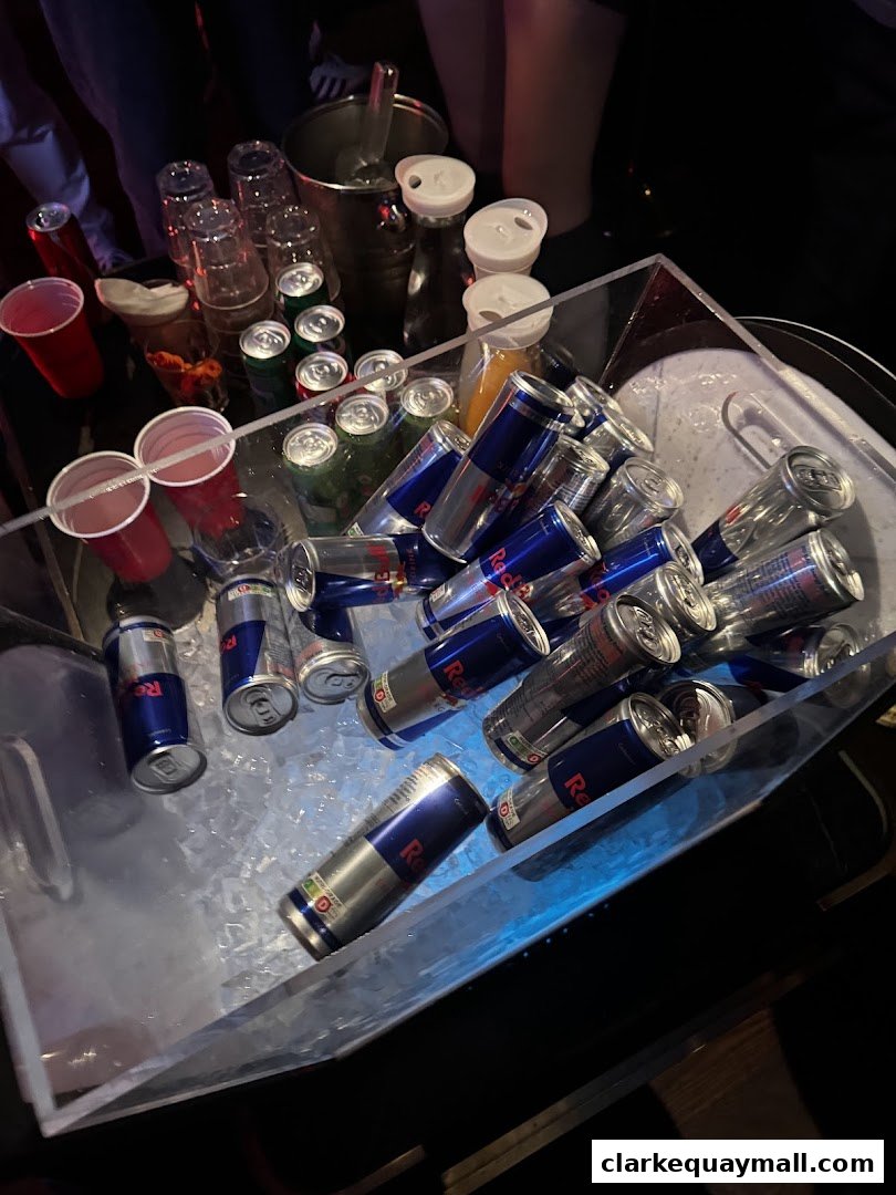 A large ice bucket filled with Red Bull cans and some glasses.