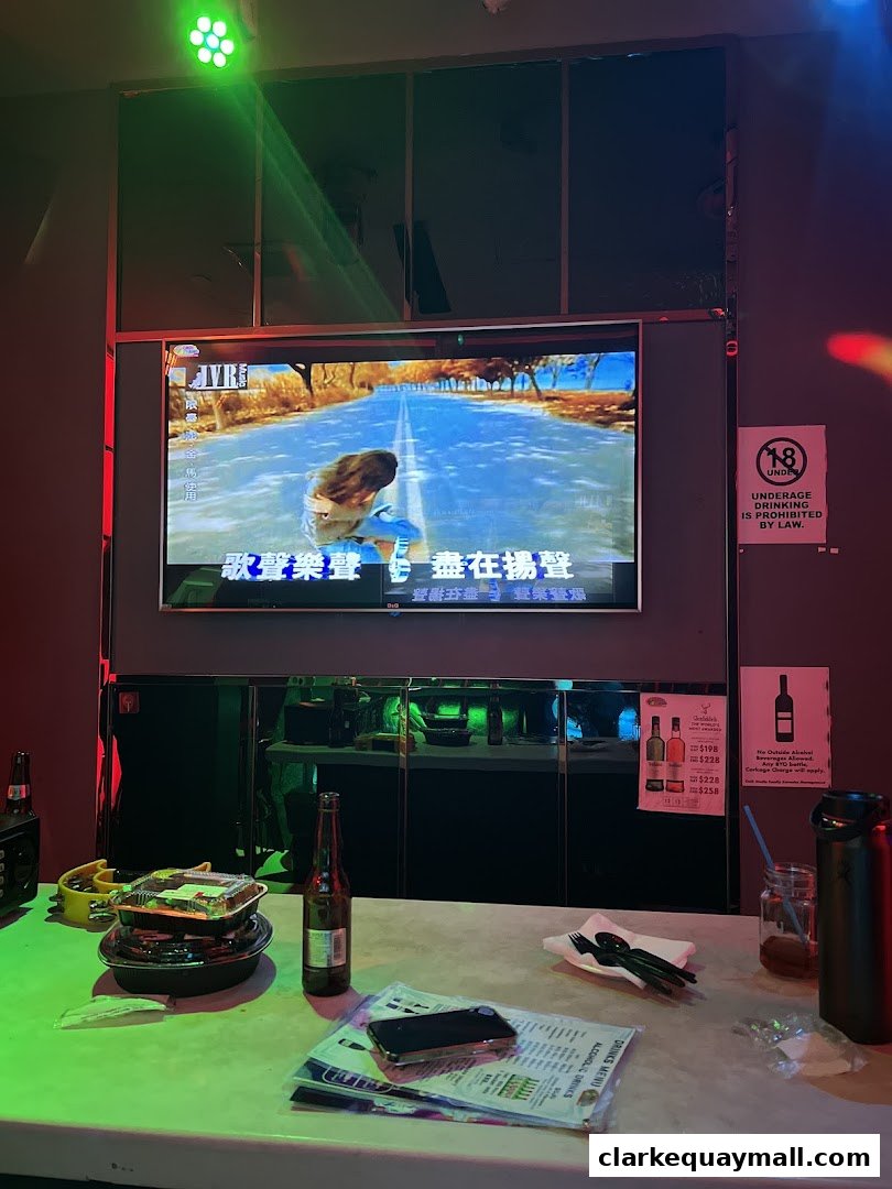 A table in a karaoke room with food, drinks, and a karaoke screen.
