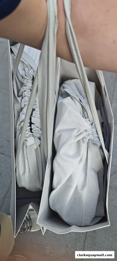A person holds two white shopping bags from Charles Keith, each containing a shoe wrapped in protective cloth.