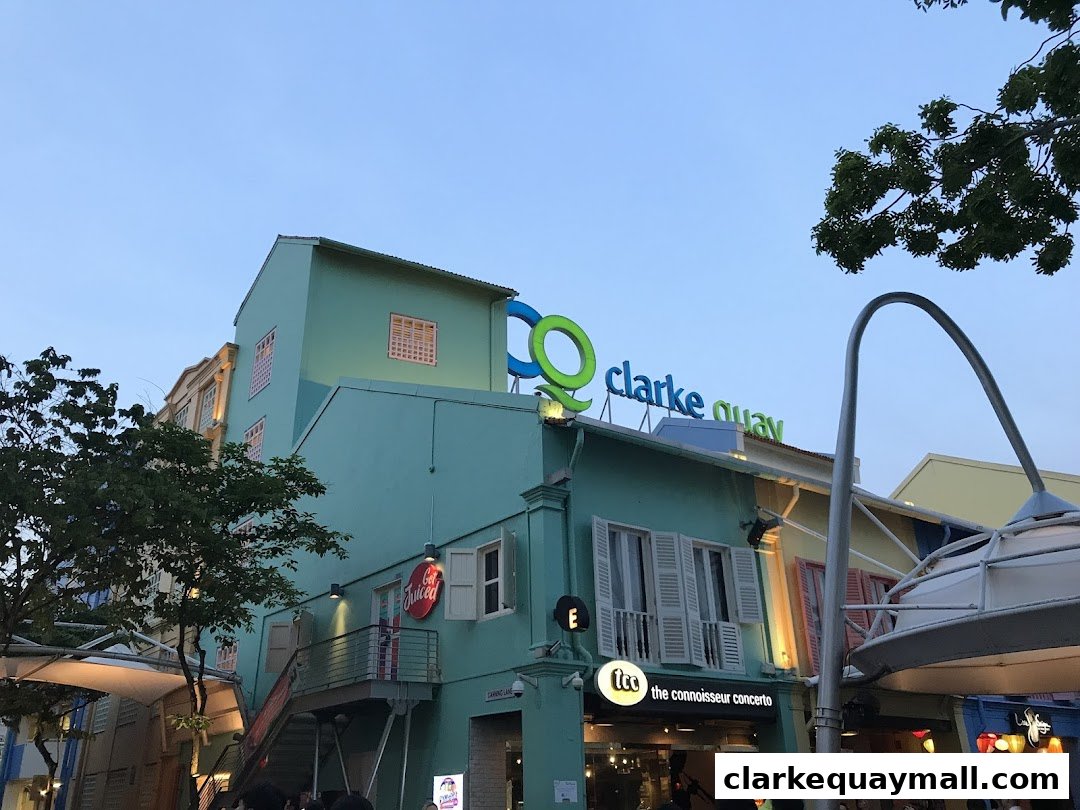 A turquoise building with "clarke quay" signage and trees against a twilight sky.
