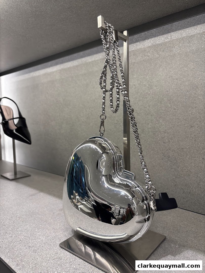 A shiny silver heart-shaped handbag with a chain strap is displayed in a store.