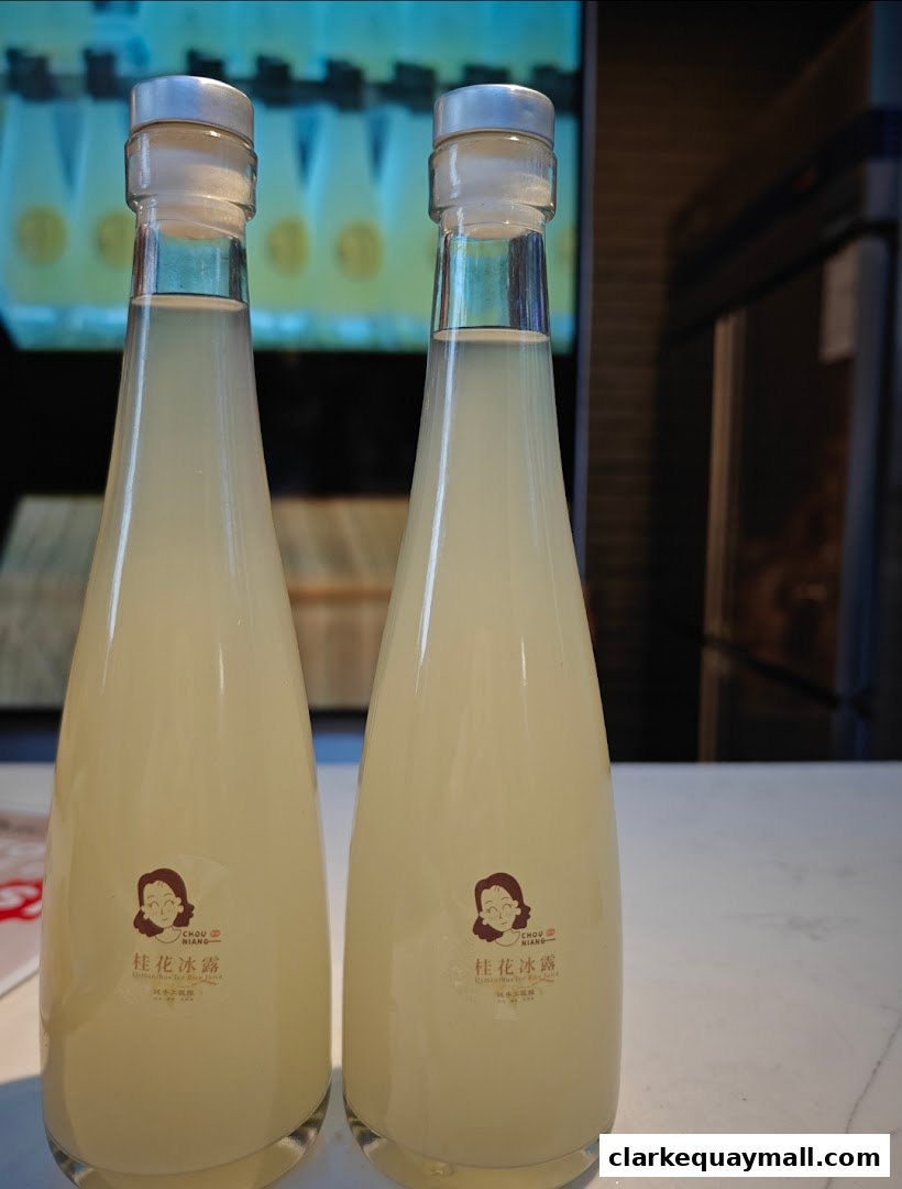 Two tall glass bottles filled with a pale yellow liquid, branded with the shop's logo.