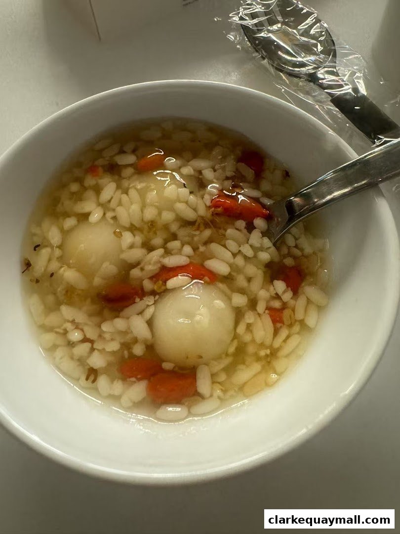 A bowl of fermented rice with glutinous rice balls and goji berries, served with spoons.