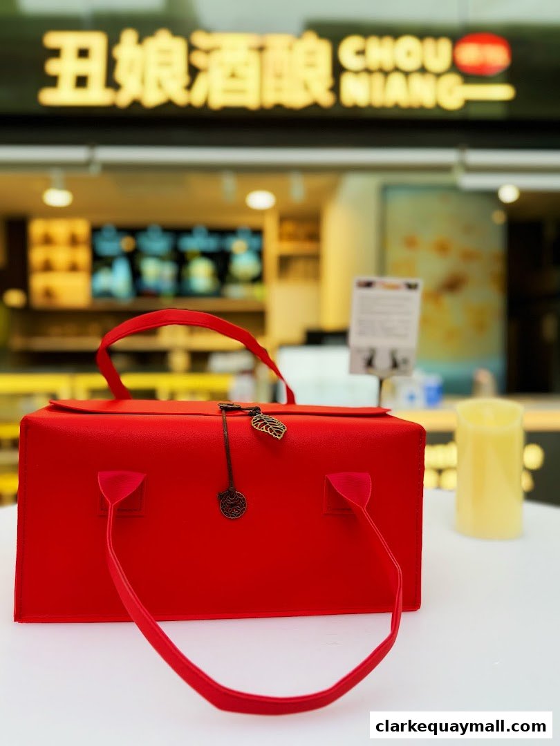 A bright red gift box with handles sits on a white table in front of a blurred shop.