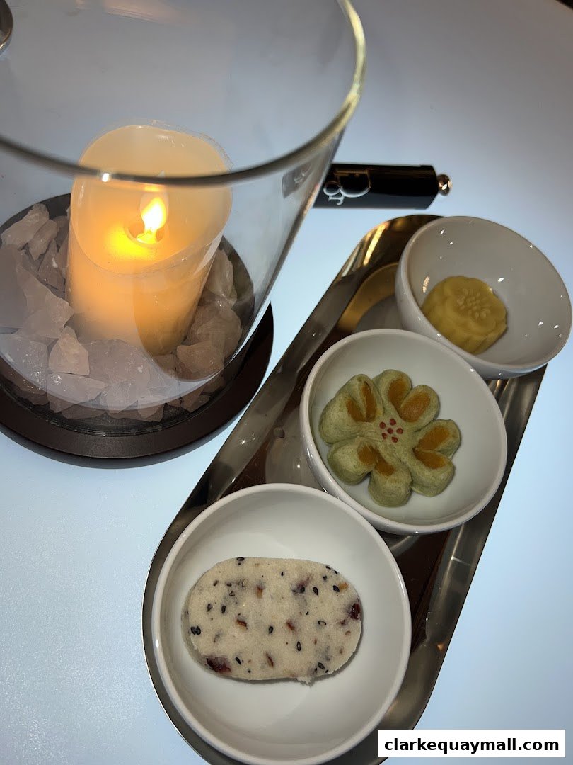 A candle illuminates a tray of three small, artfully presented desserts in white bowls.
