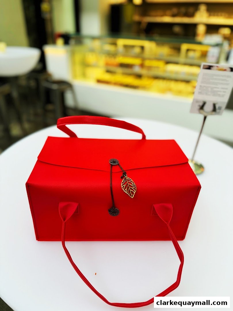 A red gift box with handles and a leaf charm sits on a white table.