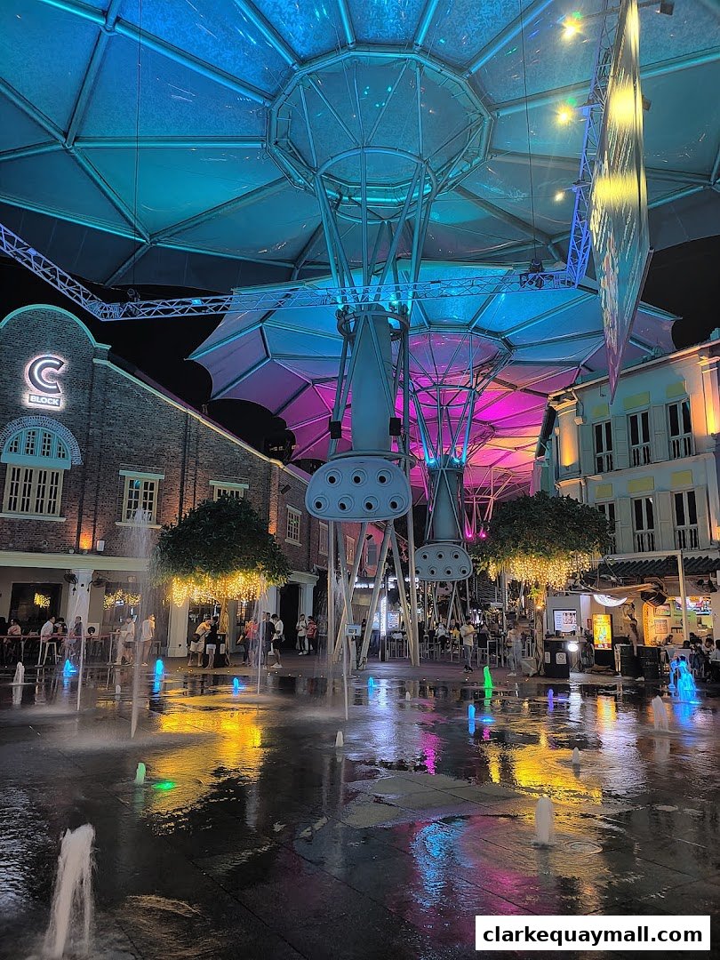 A vibrant night scene with illuminated fountains and people enjoying the atmosphere.