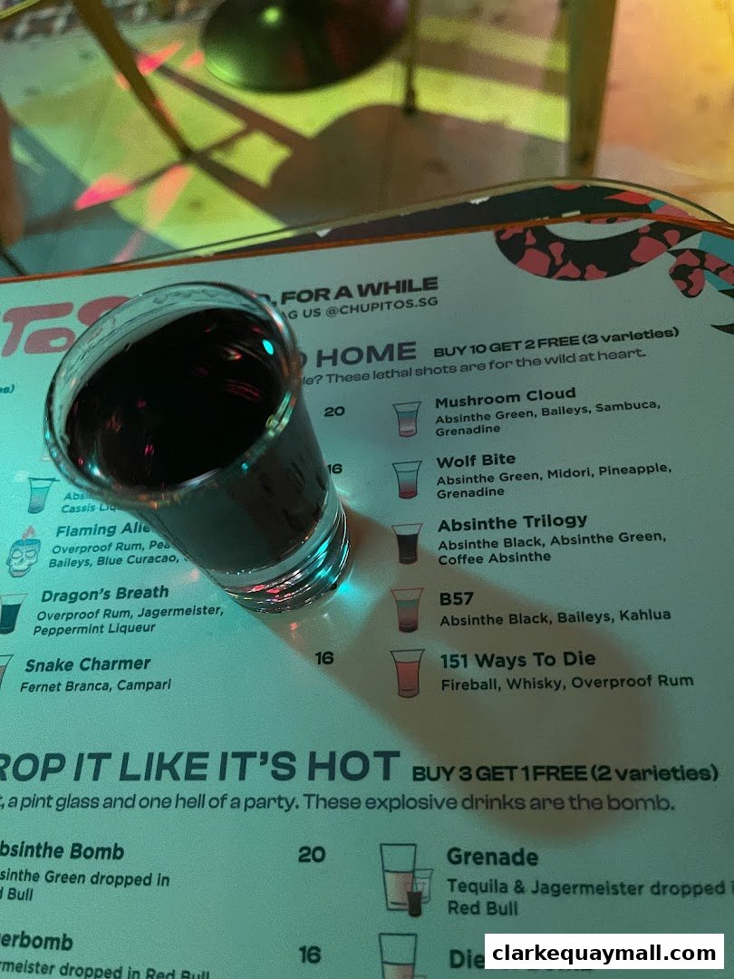 A shot glass sits on a menu featuring various colorful cocktails and drink descriptions.