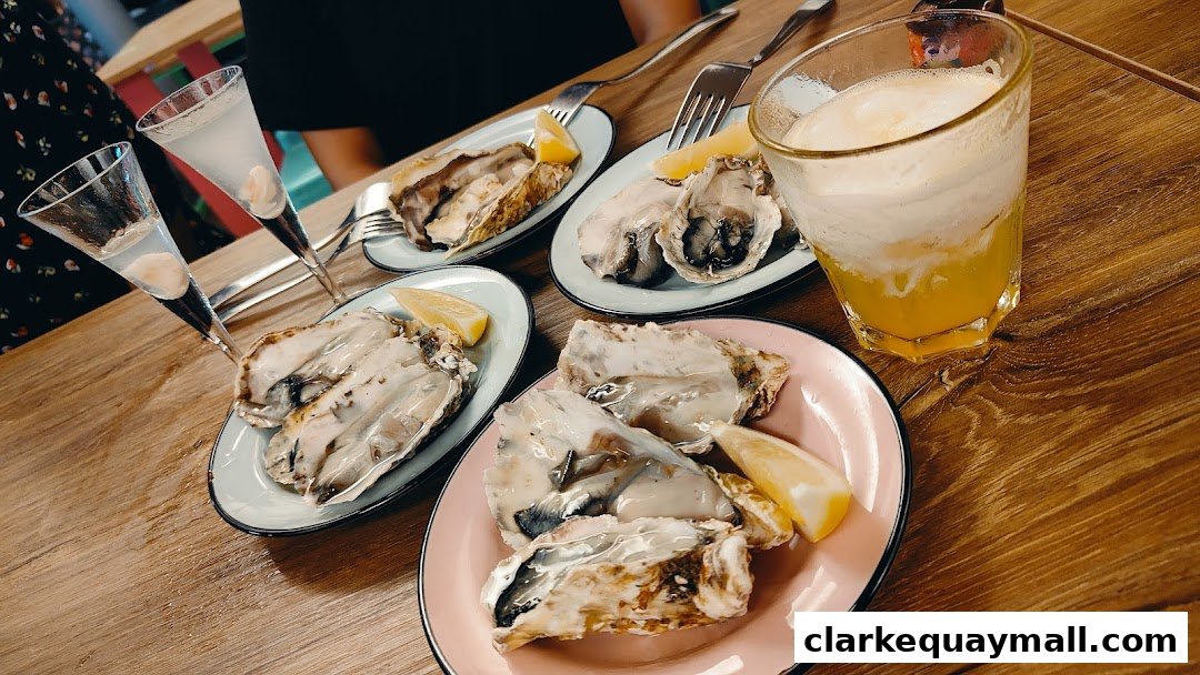 Plates of fresh oysters with lemon wedges and drinks on a wooden table.