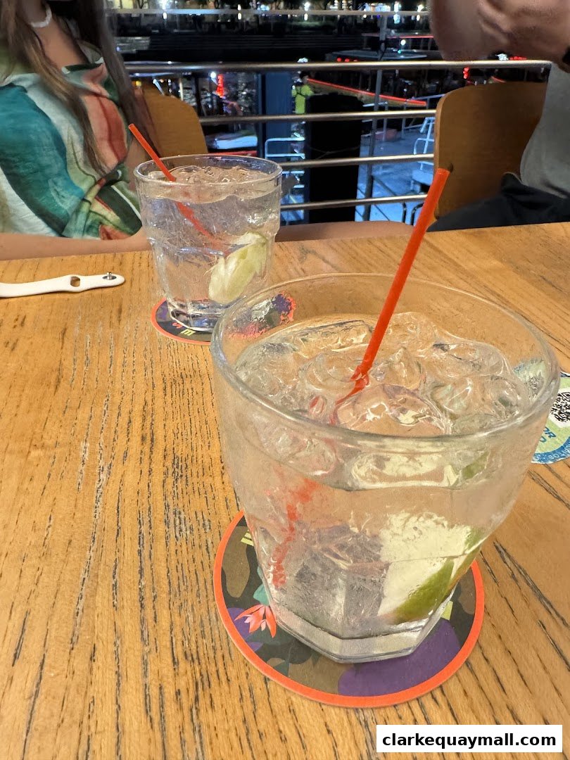Two refreshing drinks with ice and lime on a wooden table with colorful coasters.