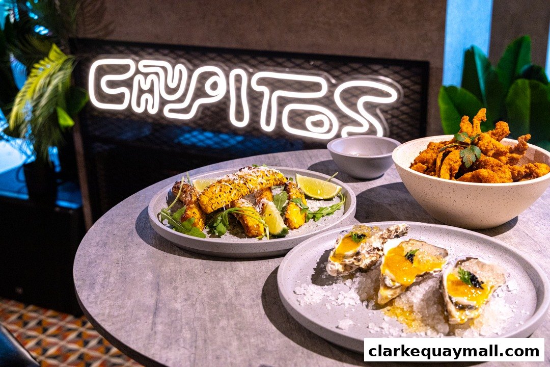 A table with three plates of food, including corn, fried seafood, and oysters, with a neon sign in the background.