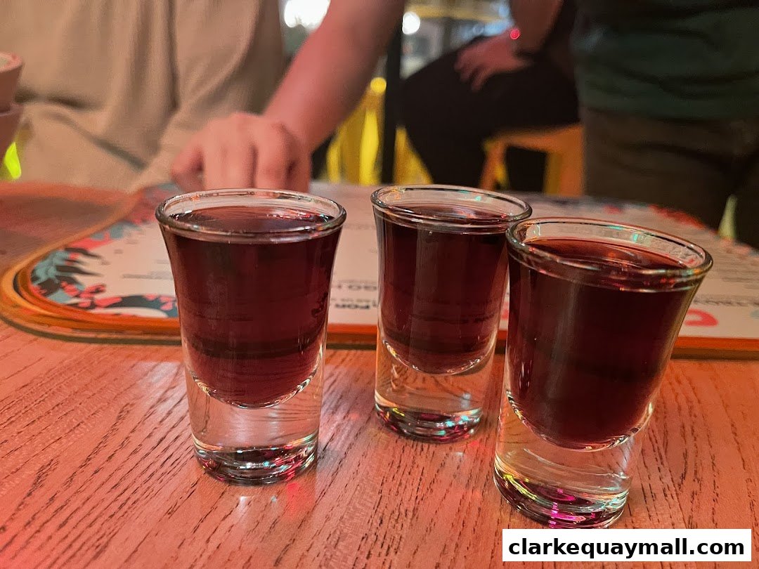 Three shot glasses filled with a dark red liquid sit on a wooden table.